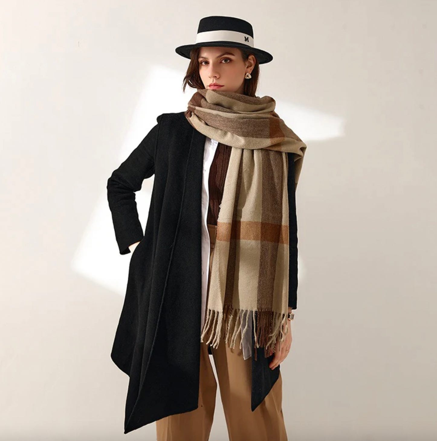 A long scarf with a large plaid pattern in shades of brown, beige, and white, featuring tassels on the ends.