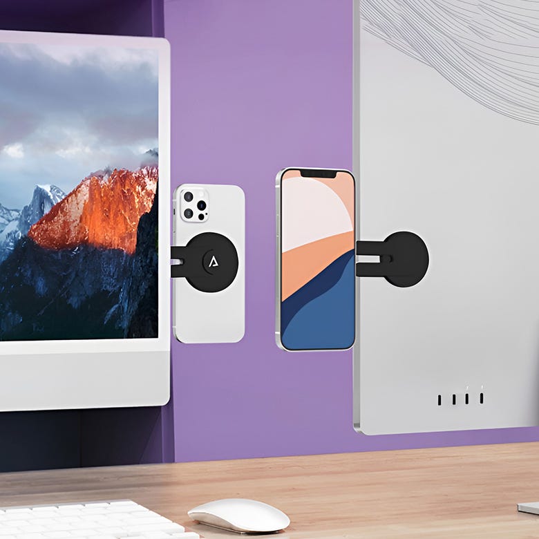 2pk Magnetic Phone Holders are small, circular mounts designed to secure phones to flat surfaces like monitors. They feature a sleek black design and are shown affixed to a computer monitor, holding a phone in place.