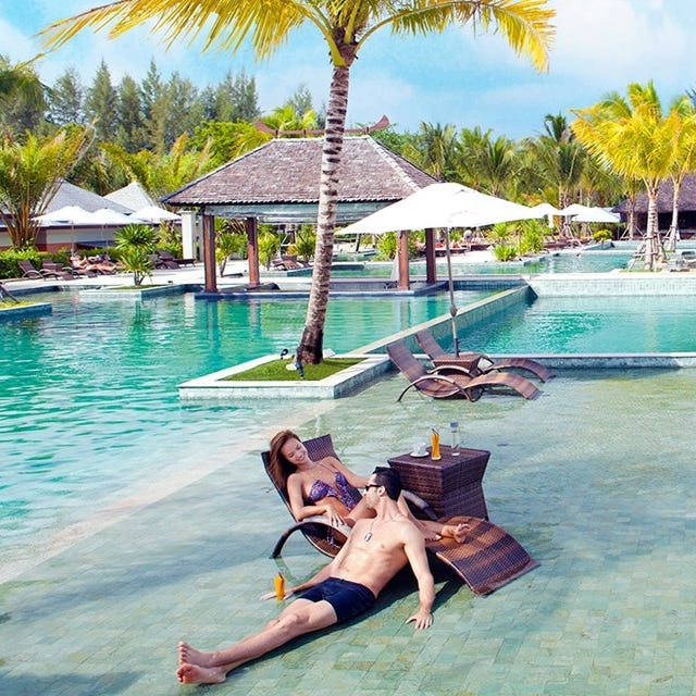 A man and woman lounging by an island resort pool with tropical surroundings.