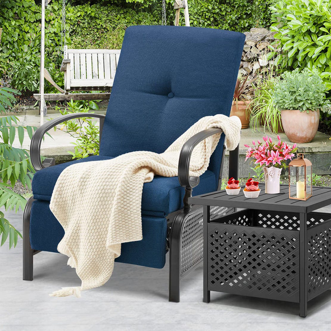 Outdoor patio setup with a blue reclining chair, cream-colored throw blanket, and a black side table displaying refreshments and a lantern.