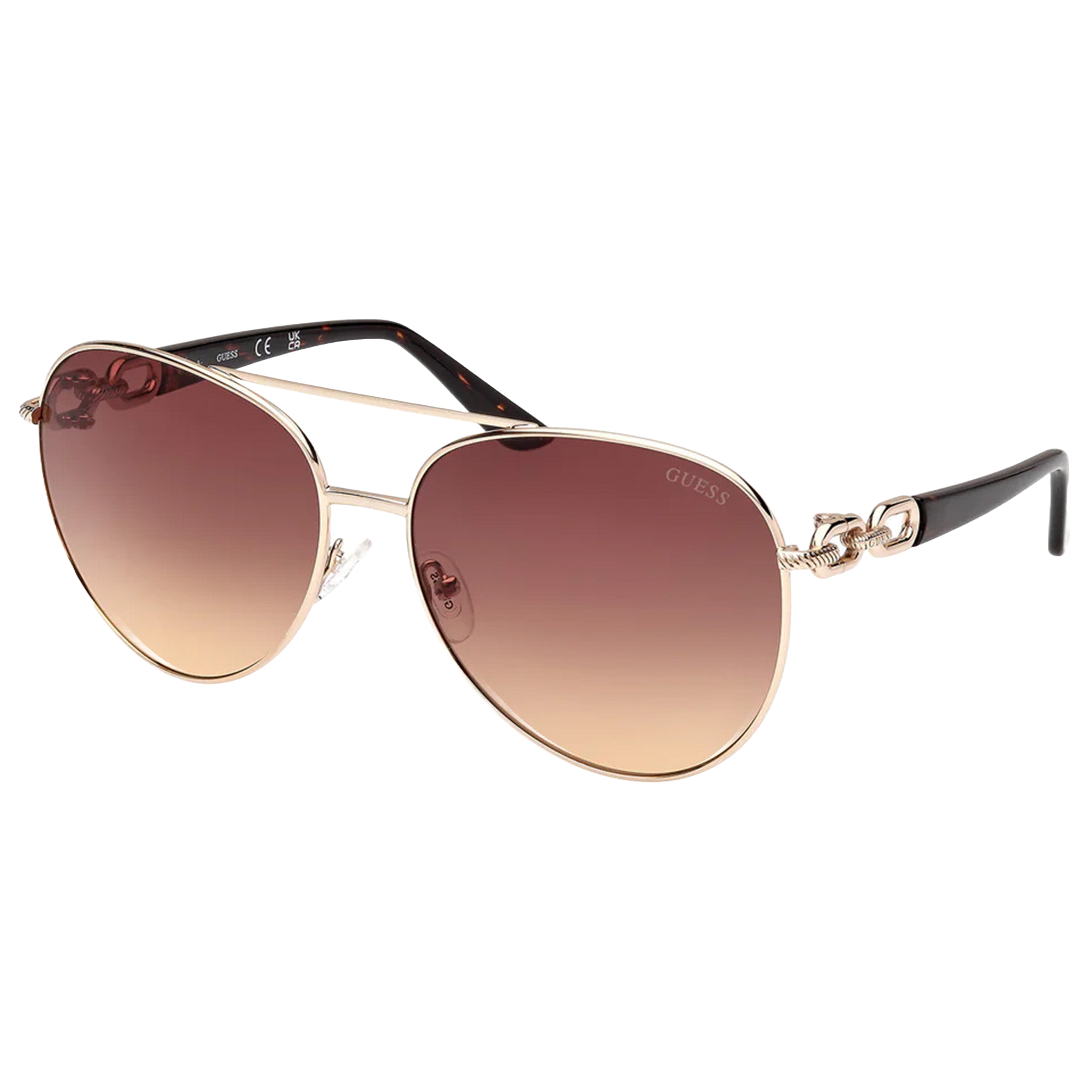 Guess aviator sunglasses with a gold-tone metal frame, gradient brown lenses, and decorative knot details on the temples. Black plastic arms add contrast and style.