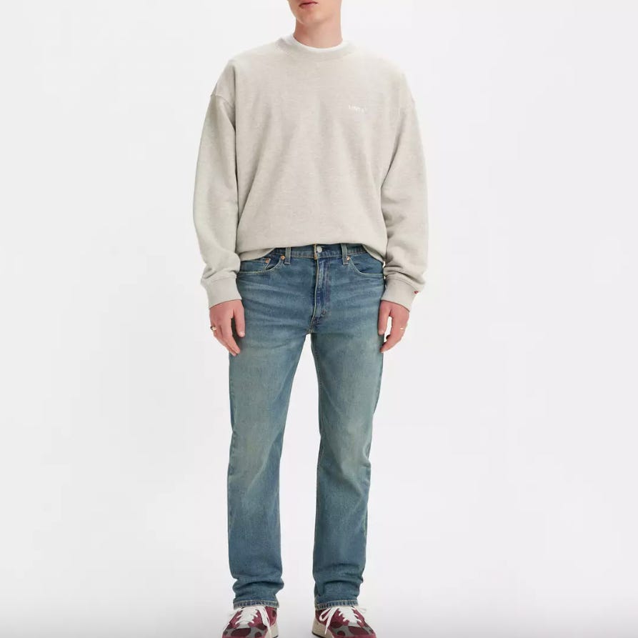 A person wearing a light grey crewneck sweater, blue jeans, and multicolored sneakers.
