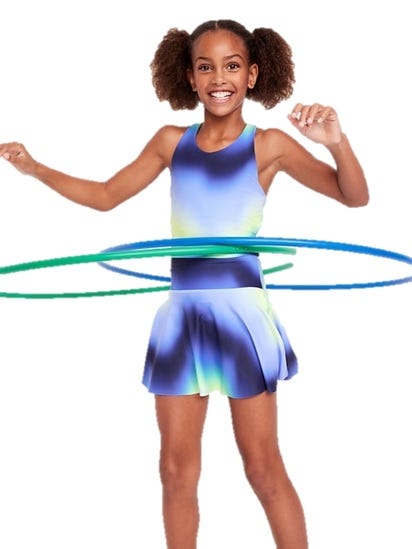 A young girl is hula hooping with two hoops, wearing a sleeveless dress with a blue, green, and white gradient.