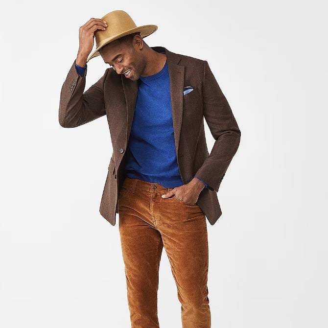 A man wearing a brown blazer, blue sweater, corduroy pants, and a straw hat.