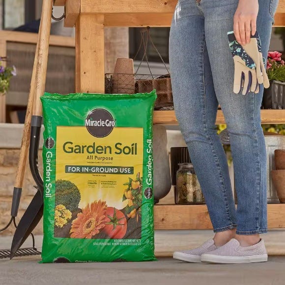 A bag of Miracle-Gro Garden Soil and gardening tools with a person standing nearby.