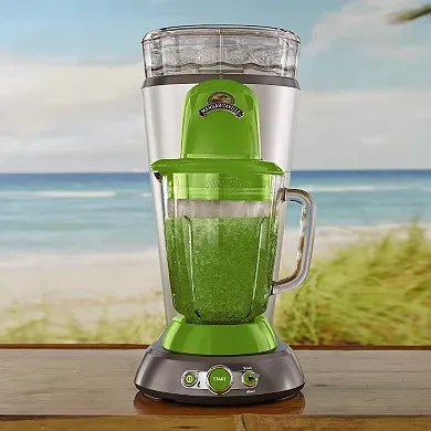 A green and grey Margaritaville branded drink maker with a large clear blending jar full of a green blended beverage, set against a beach backdrop.