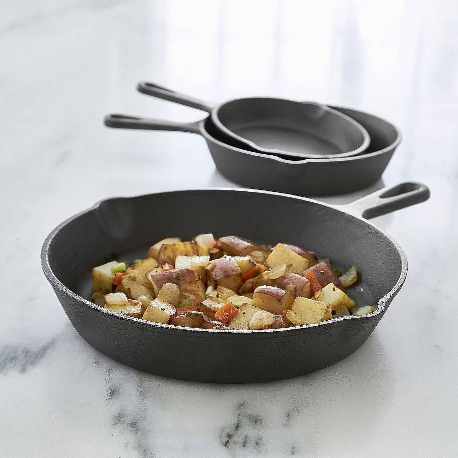 Two black cast iron skillets on a marble surface, one containing cooked vegetables and sausage.