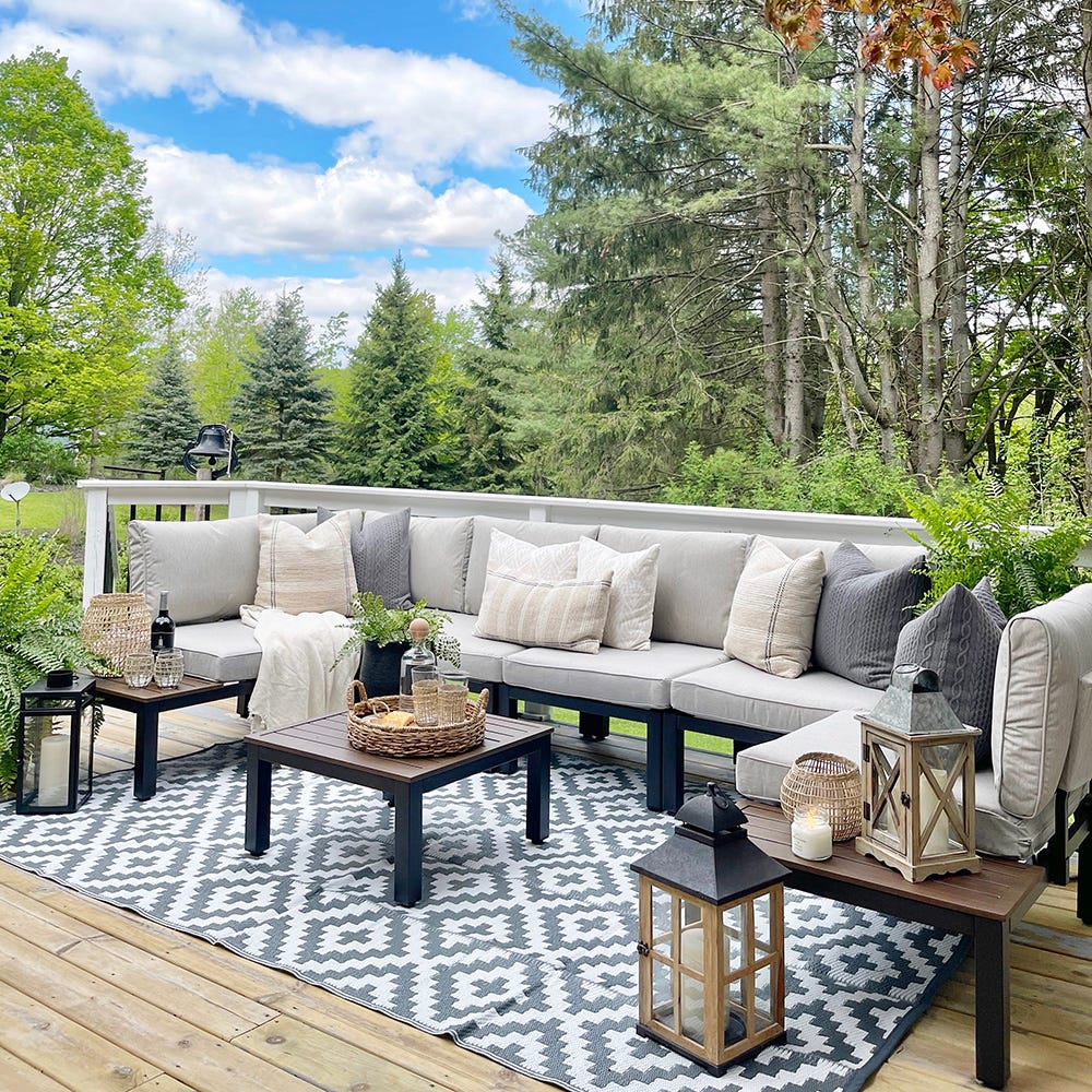 Outdoor furniture set with sectional sofa, coffee table, lanterns, and patterned rug on a wooden deck.