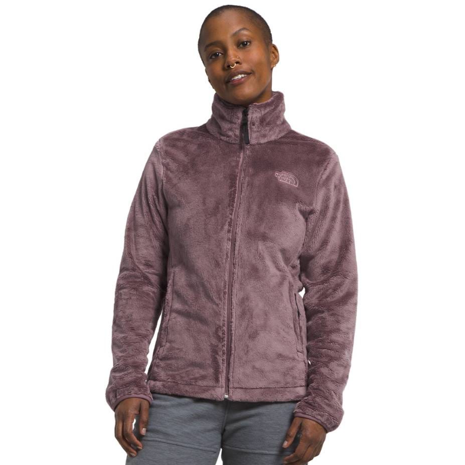 A mauve zip-up fleece jacket from The North Face with a high collar, featuring the brand's logo on the chest. The material appears soft and plush, designed for warmth and comfort.