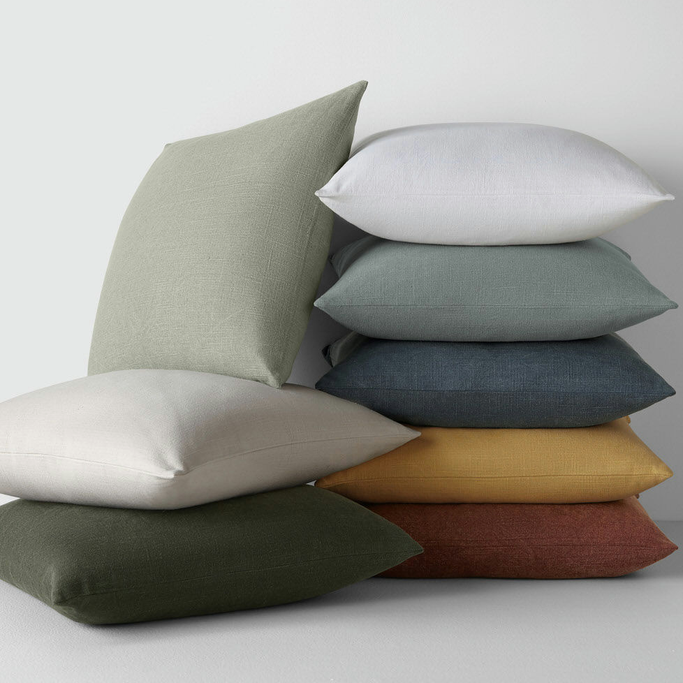 A stack of seven assorted throw pillows in various solid colors.
