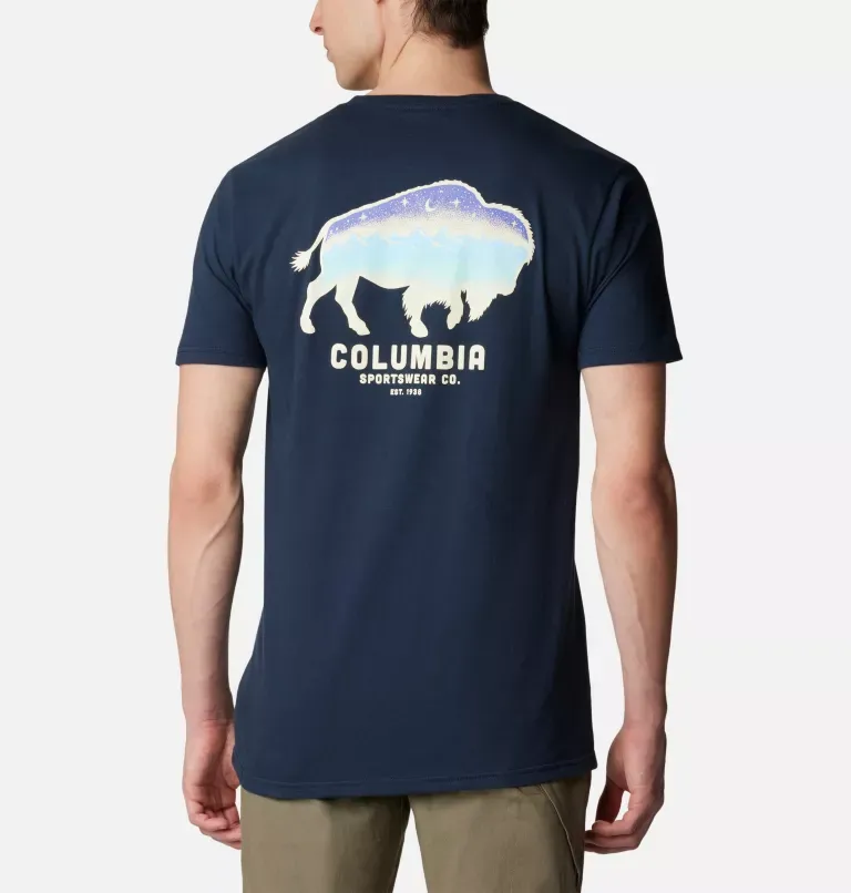 A man is wearing a navy-blue T-shirt with a white silhouette of a buffalo filled with a mountain and night sky design, accompanied by a branded logo text beneath it.