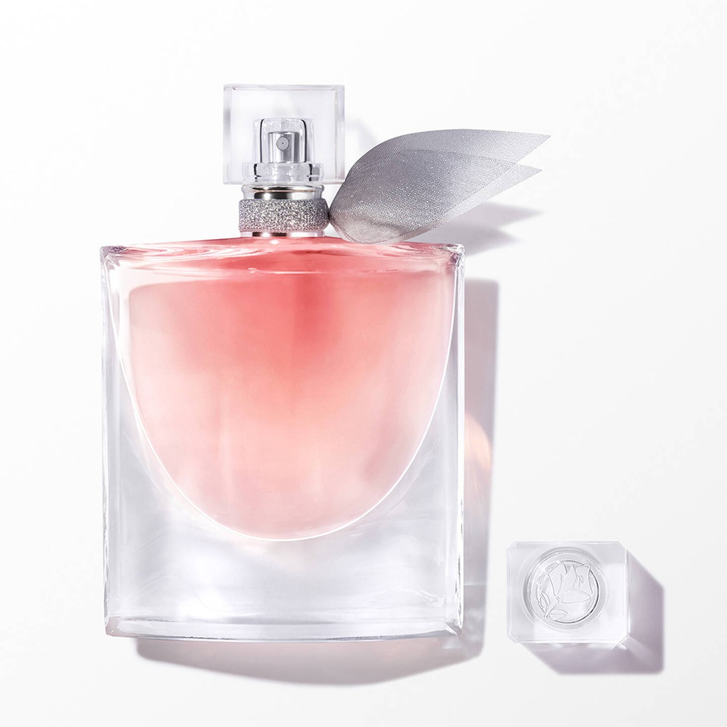 A rectangular glass perfume bottle with a light pink liquid and a silver-gray ribbon decoration on the cap.