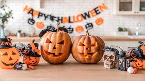 Pumpkins, carved into Jack o Lanterns, on a table with a Halloween banner in the background.
