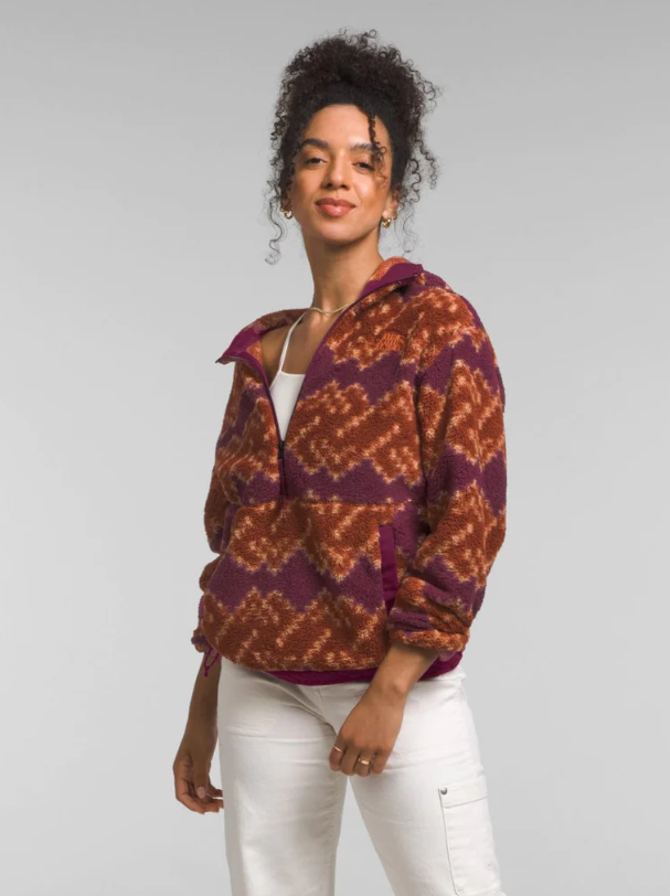 A woman is wearing a patterned zip-up fleece jacket in purple and orange, paired with white pants.