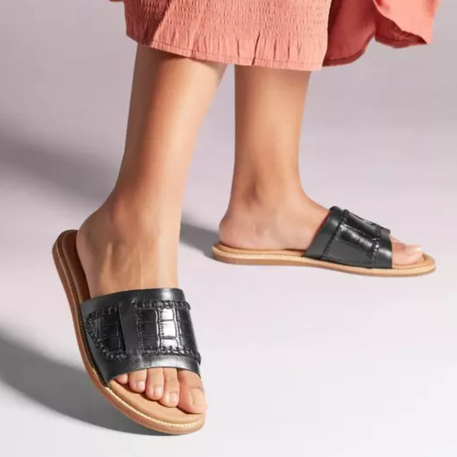 A pair of black slide sandals with a wide strap, worn with a pink skirt.