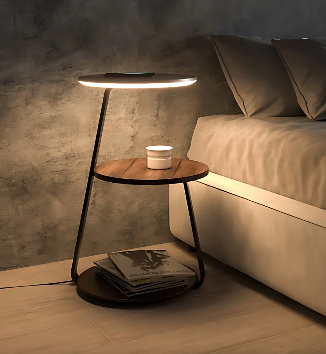 A bedside table with a round wooden top and a circular light above it; there's also a storage tray underneath holding magazines.