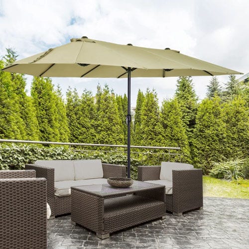An outdoor patio set with a large umbrella, a sofa, two chairs, and a table on a paved area surrounded by greenery.