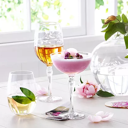 Various glasses containing drinks and a decorative glass bowl, on a table with floral embellishments.