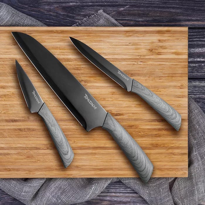 Three black kitchen knives with textured grey handles on a wooden cutting board.