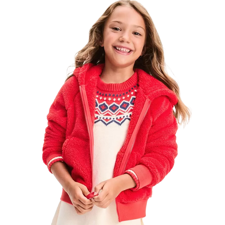 A red fleece zip-up hoodie with a cozy texture features a front zipper and side pockets, worn over a cream sweater with a red and blue geometric pattern on the chest.