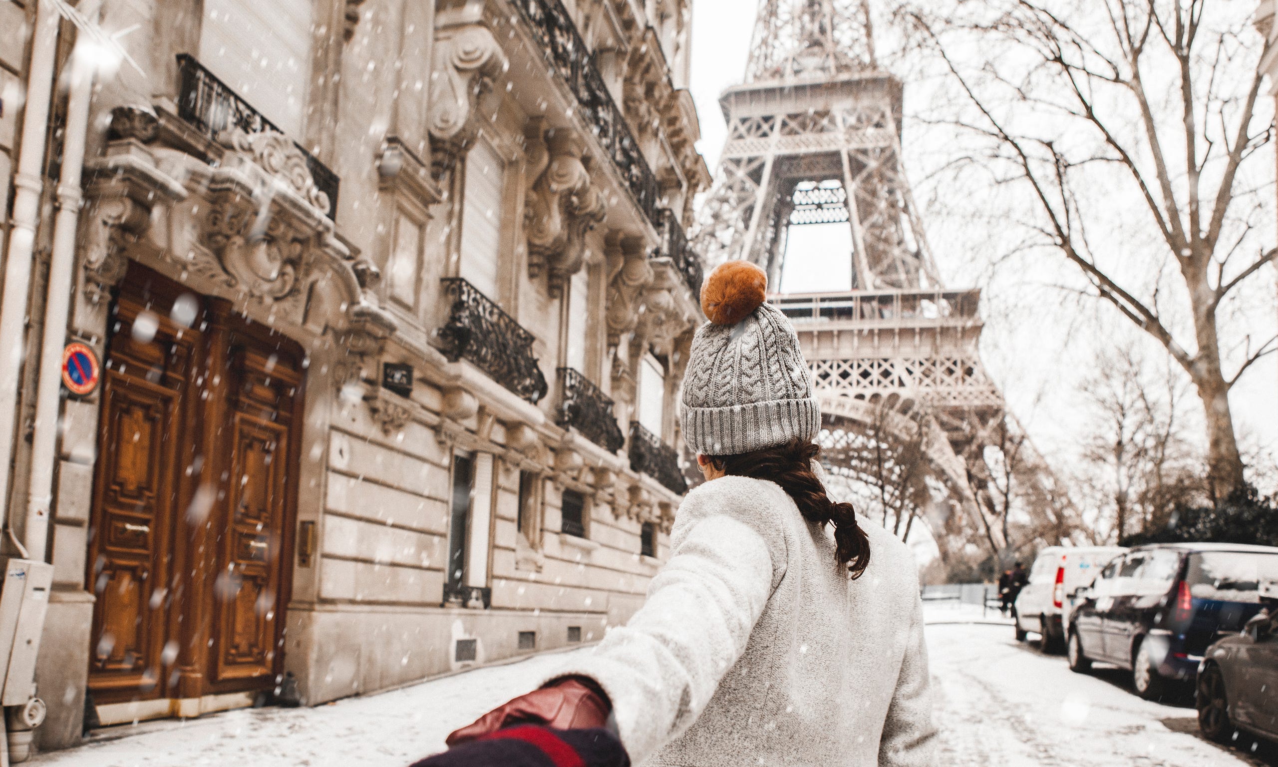 A person with insider tips on holiday travel walks in the snow in Paris, with the Eiffel Tower in the background.