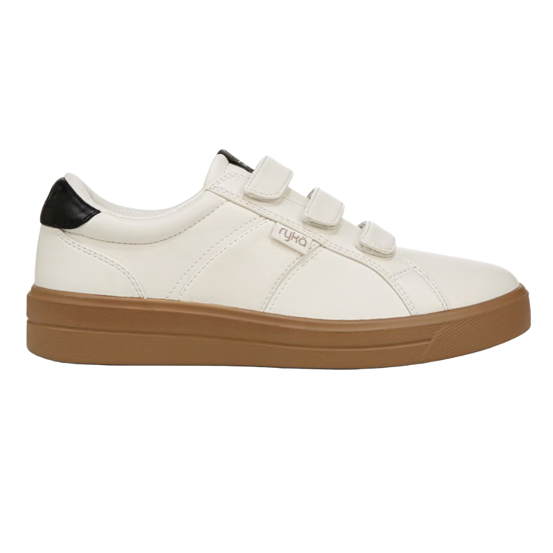The Ryka Viv Classic Shoes are white sneakers with three Velcro straps, featuring a contrasting black heel detail and a brown rubber sole. They have a casual and sporty design.
