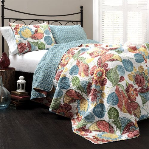 A quilt and pillow sham set featuring a floral pattern in vibrant reds, blues, and yellows on one side and a light blue geometric pattern on the reverse.