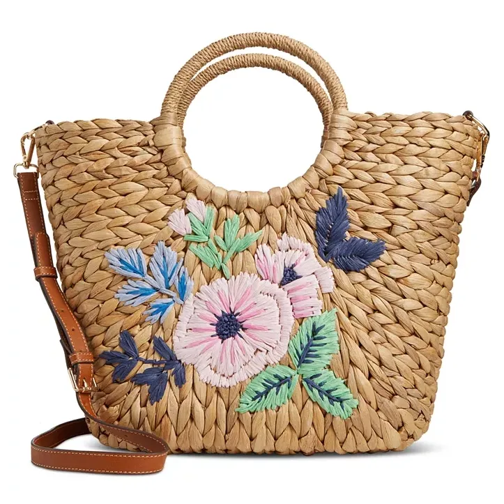 Woven straw tote bag with embroidered floral pattern and circular handles, equipped with a detachable leather shoulder strap.