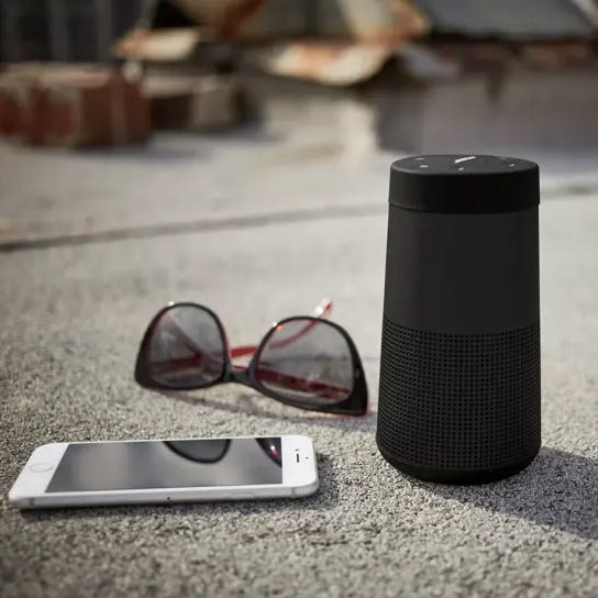 Smart speaker, smartphone, and sunglasses on a concrete surface.