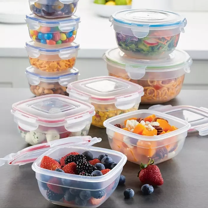 Various sizes of clear plastic food storage containers with colorful lids, some stacked and some filled with fruits, salad, and snacks.
