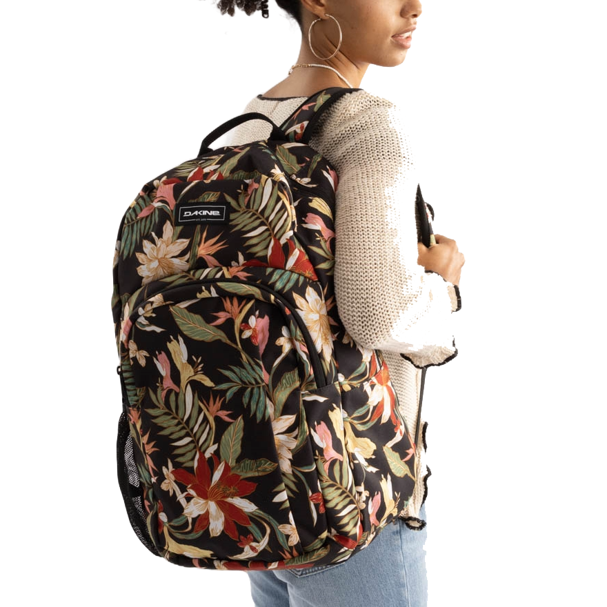 A person is wearing a Dakine backpack with a floral pattern, featuring multiple compartments and mesh side pockets.