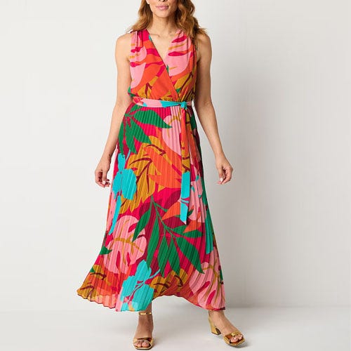 A woman wearing a colorful sleeveless maxi dress with a wrap design and a tropical print, paired with gold sandals.