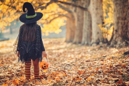 A child in a witch costume trick or treating outdoors in autumn.