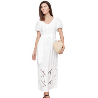 A woman in a white dress with puff sleeves and a lace hem detail holds a woven clutch.