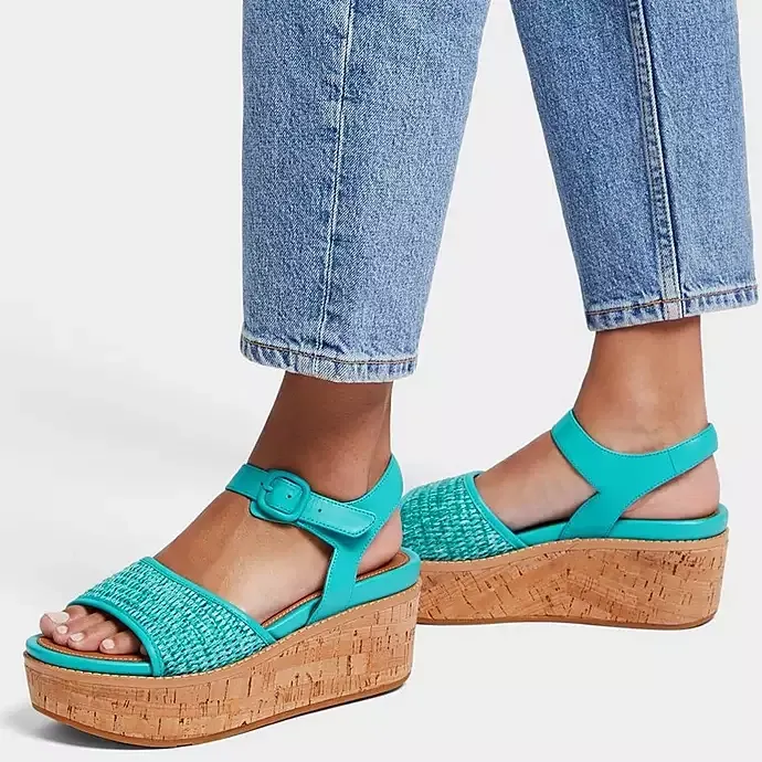 A pair of teal platform sandals with woven straps and cork heels, worn with cuffed blue jeans.