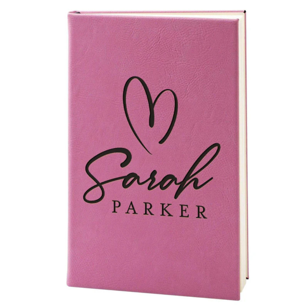 A pink hardcover journal features the name \“Sarah Parker\“ with a stylized heart above it.