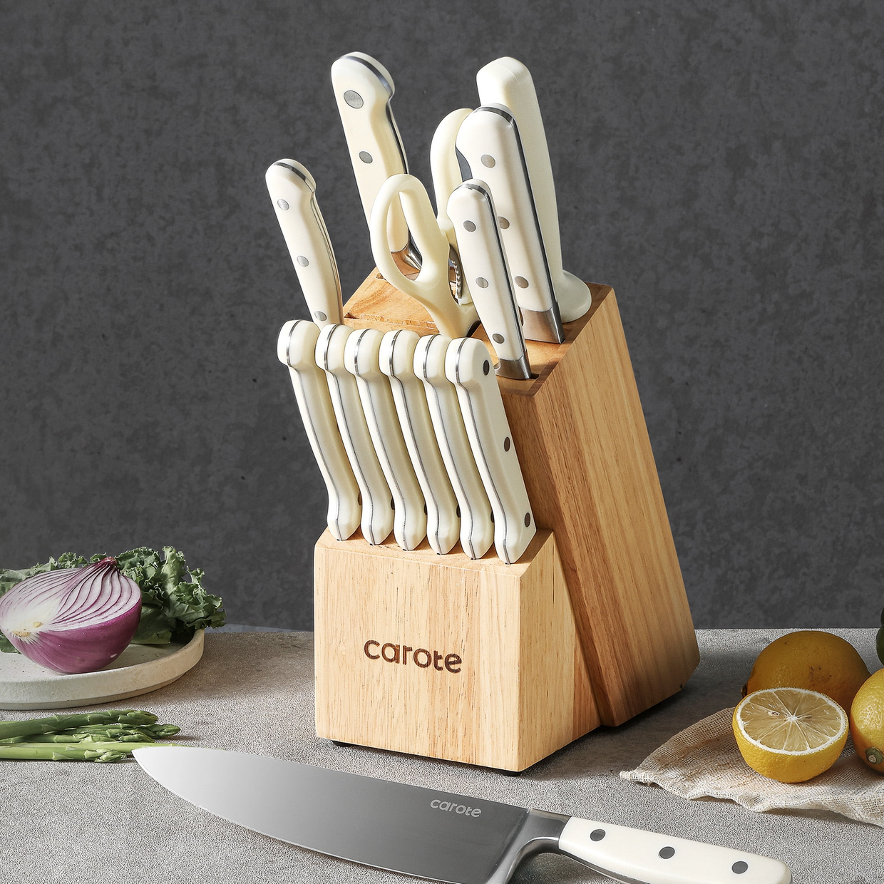 A set of white-handled kitchen knives in a wooden block, with vegetables and a knife on a countertop.