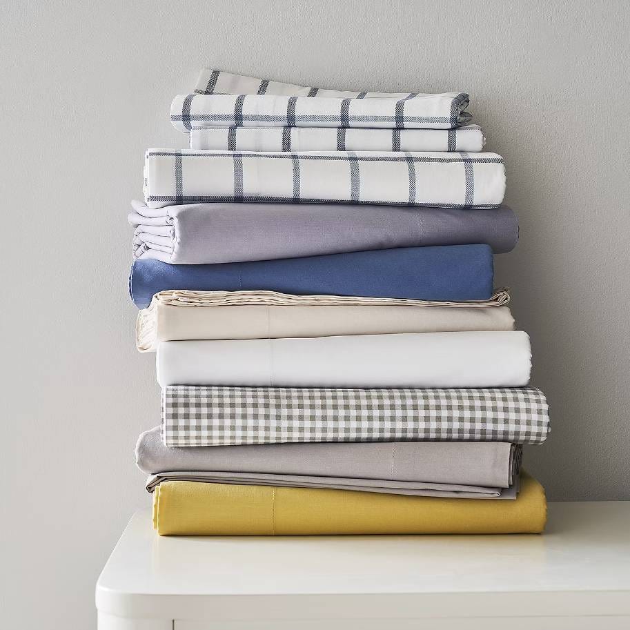 A stack of folded textiles in various colors and patterns, including plaids and solids.