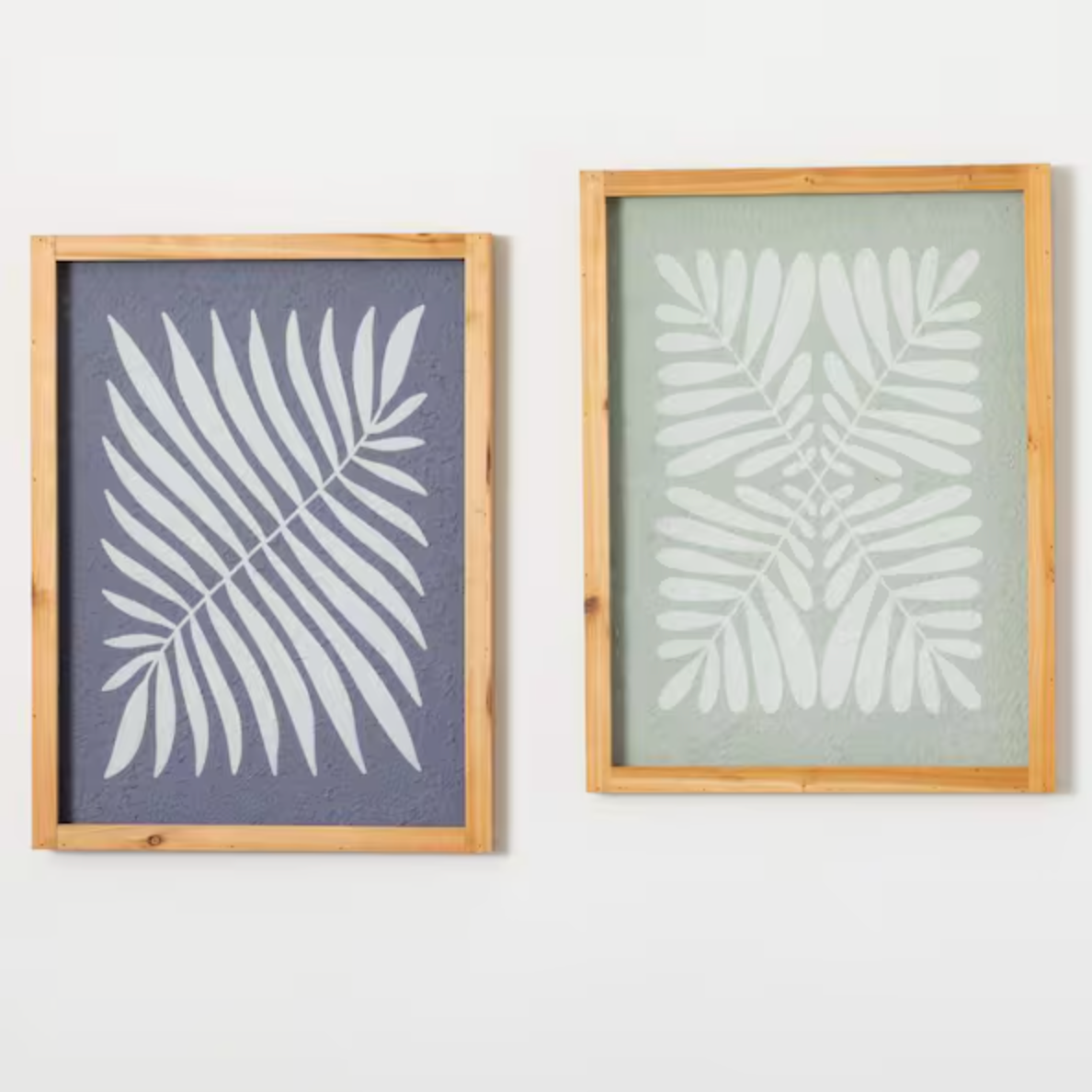 Two framed pieces of art featuring abstract leaf designs, one with a dark blue background and the other with a light green background.