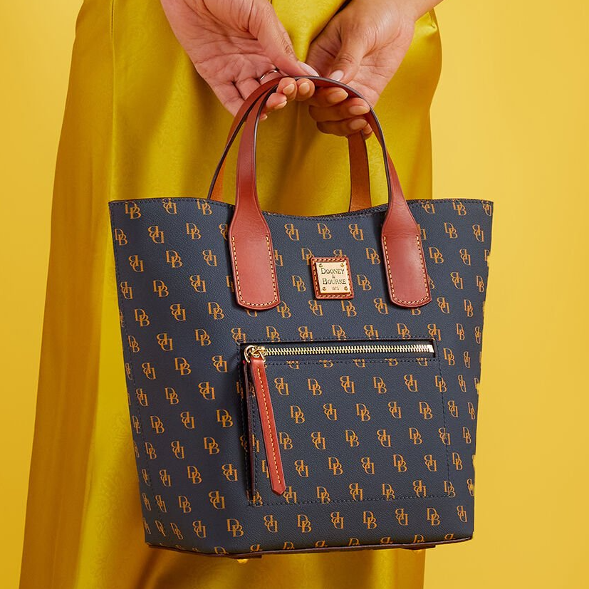 A navy blue tote bag with a tan handle and monogram print, featuring an external zip pocket.