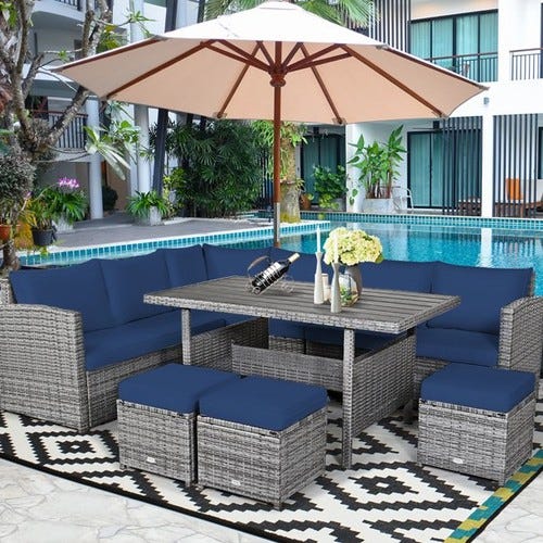 Patio set with wicker seats, blue cushions, a table, and a large umbrella by a pool.