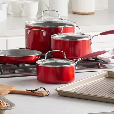 A set of glossy red ceramic cookware, including two saucepans with lids, a stockpot with lid, two frying pans, and a baking tray.