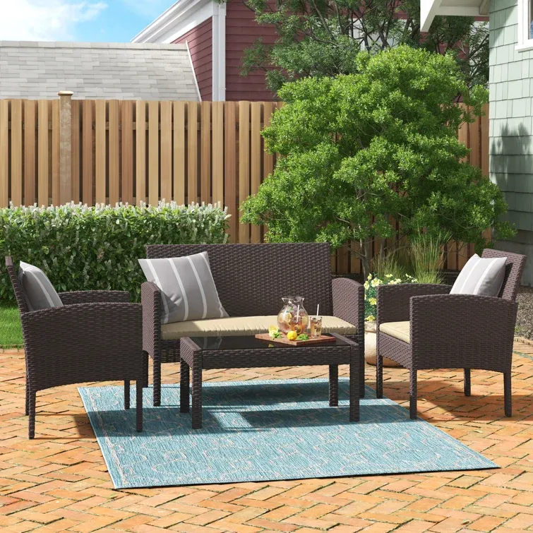 A brown outdoor furniture set consisting of a two-seater sofa, two chairs, and a rectangular coffee table, on a blue and cream rug.