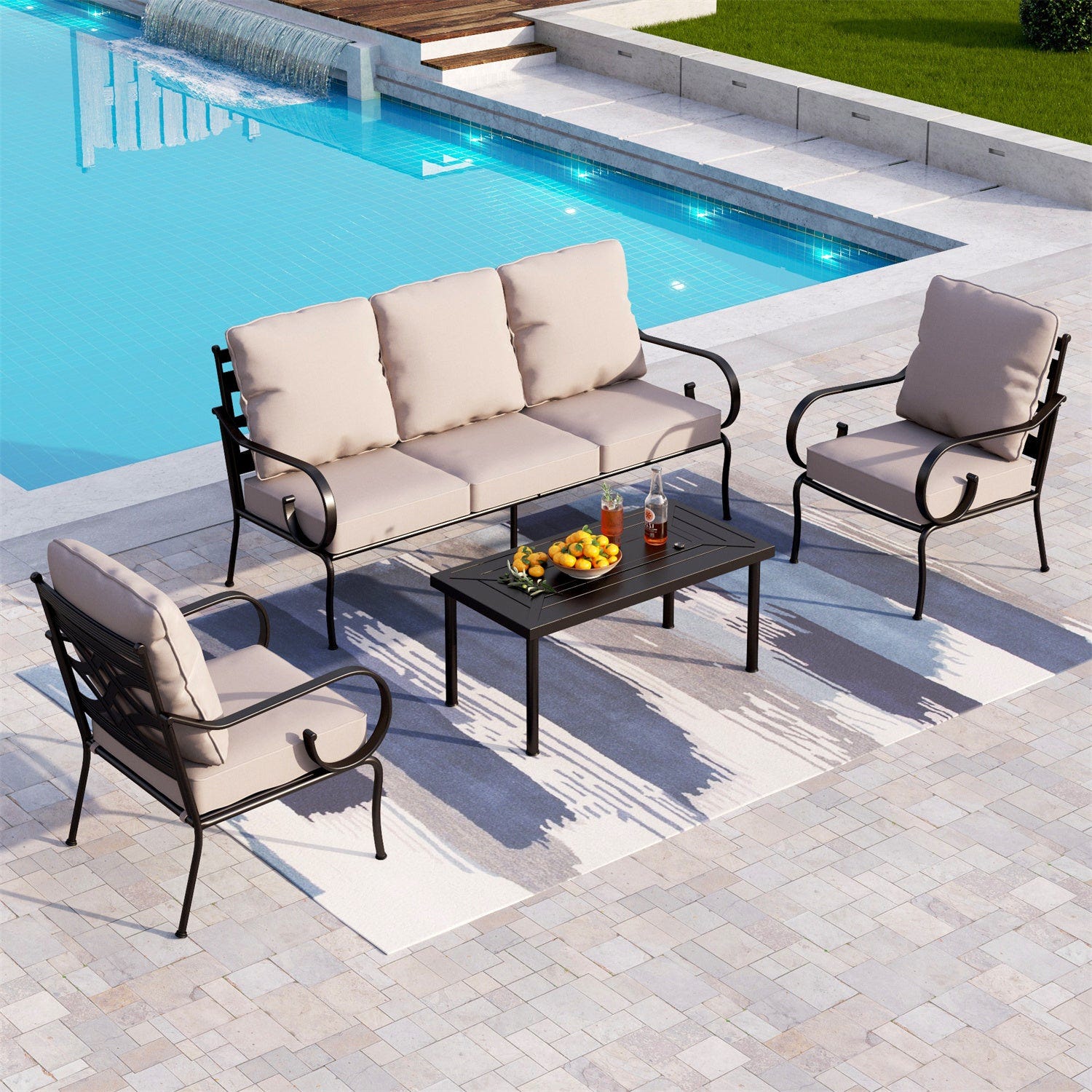 A four-piece patio set including a three-seater sofa with beige cushions, two matching armchairs, and a rectangular coffee table, arranged on a patterned outdoor rug by a pool.
