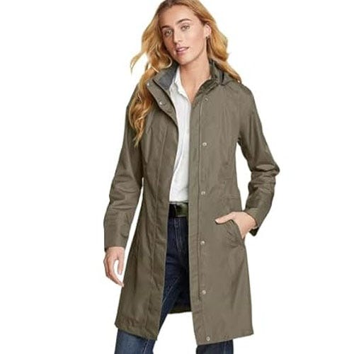 A woman is wearing a long, olive-green trench coat over a white shirt and blue jeans.
