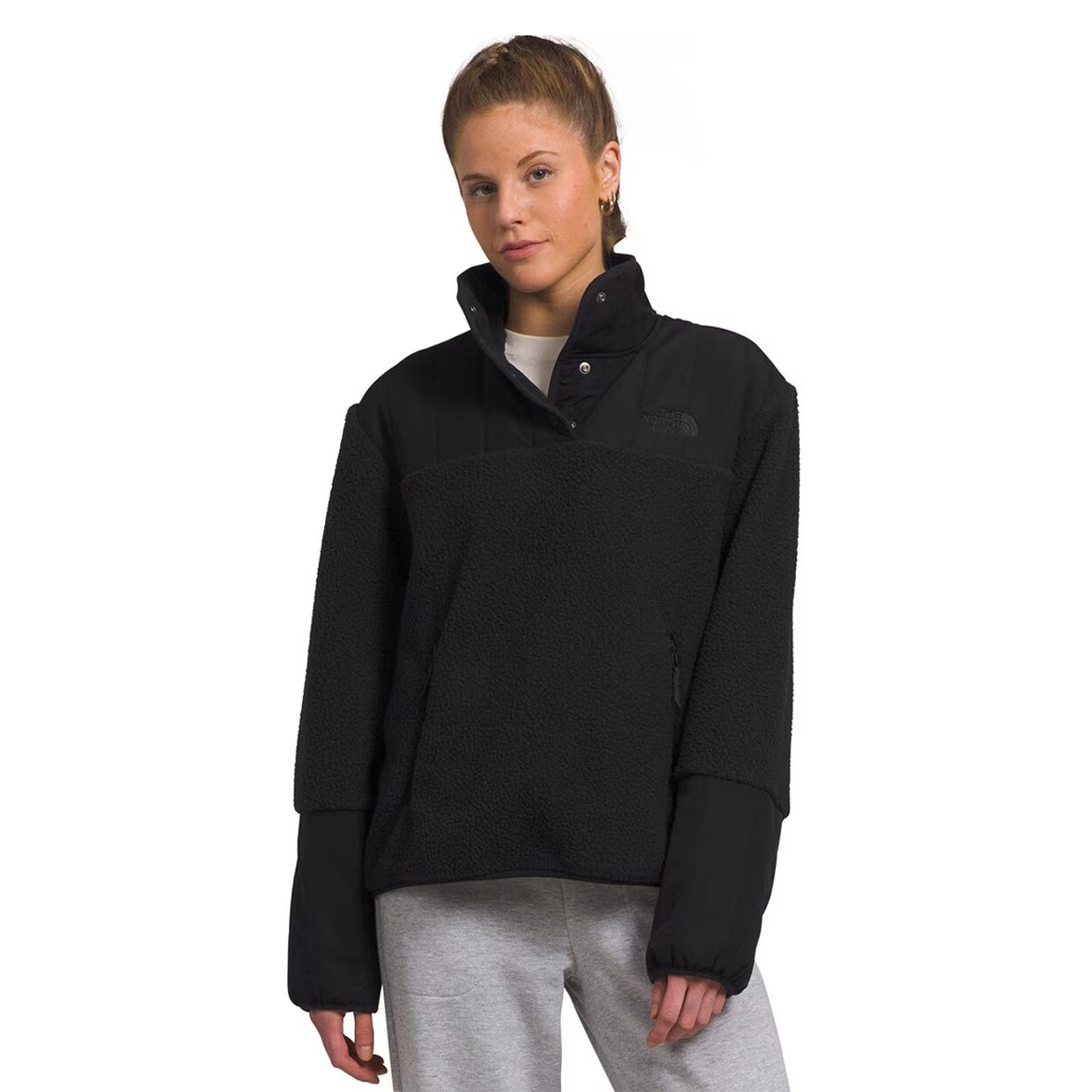 A woman is wearing a black North Face Cragmont Fleece, featuring a snap-button collar, sherpa-like texture, and a relaxed fit, paired with gray sweatpants.