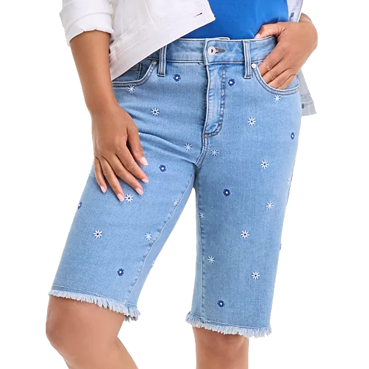 Light blue denim Bermuda shorts with frayed hems, featuring scattered white and blue embroidered daisies. The shorts have front and back pockets, belt loops, and a button-and-zip closure.