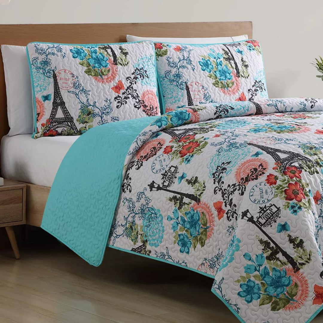 A colorful quilted bedspread with matching pillowcases, featuring floral patterns and Eiffel Tower motifs.