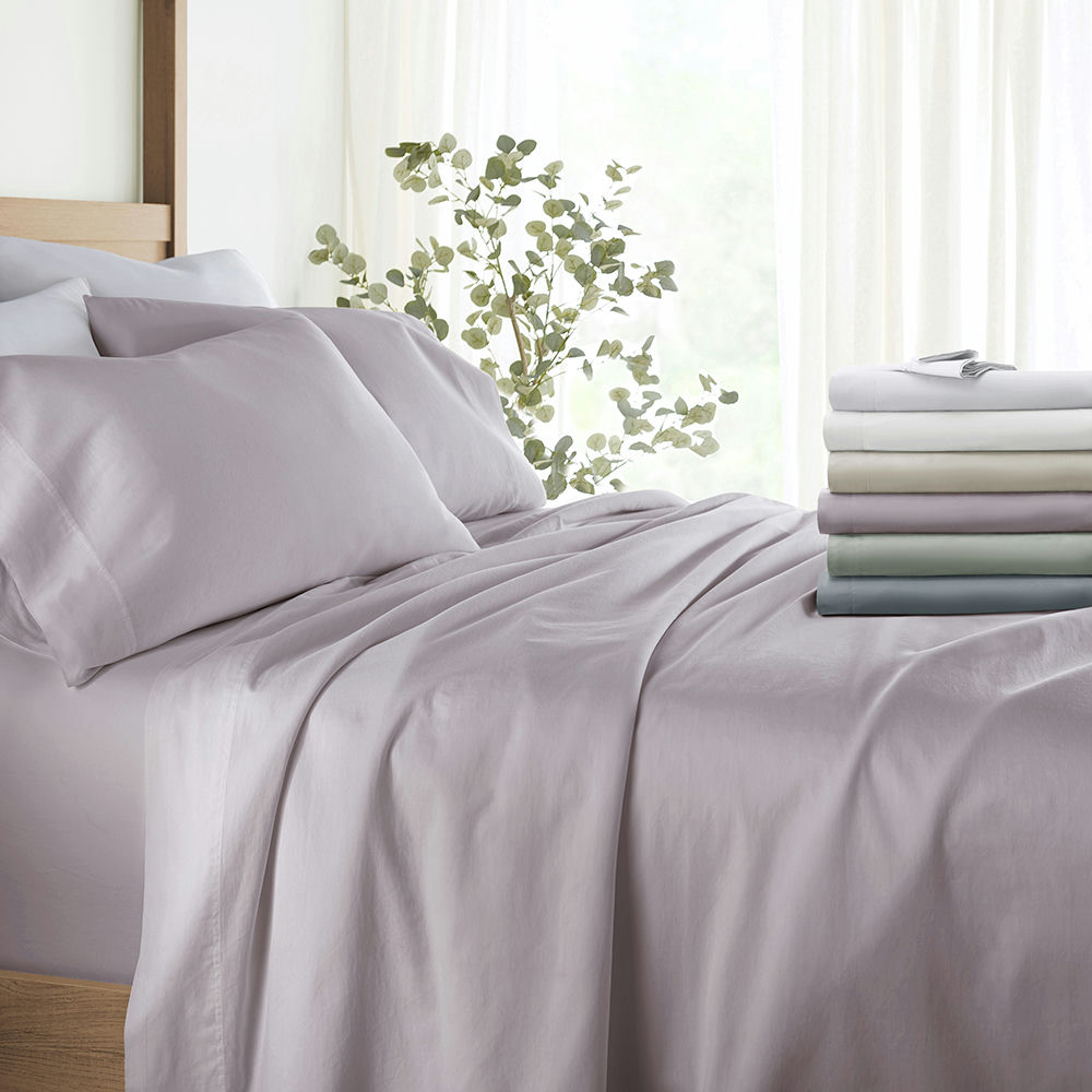 Bedding set comprising sheets and pillowcases in a range of pastel colors, displayed on a bed and stacked to the side.