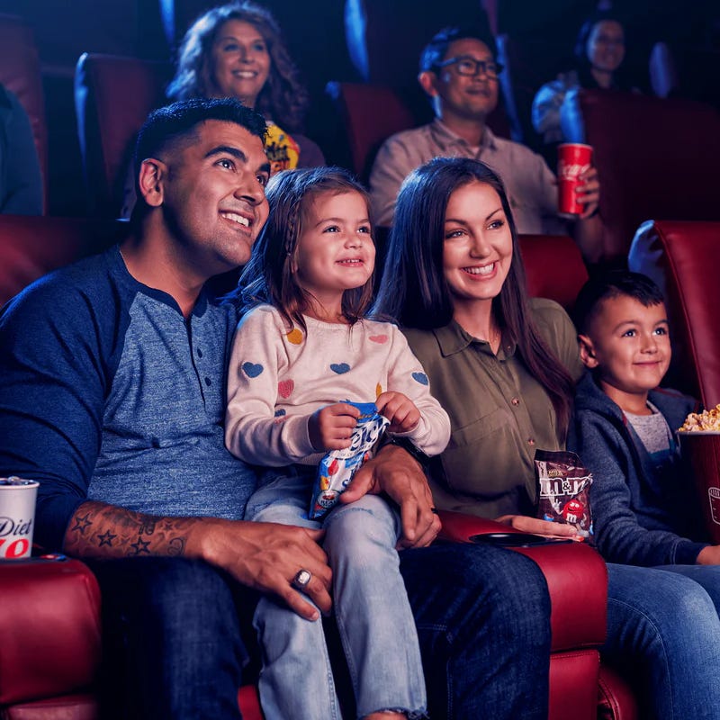 A family is enjoying a movie, holding Diet Coke, M&M's, and Skittles.